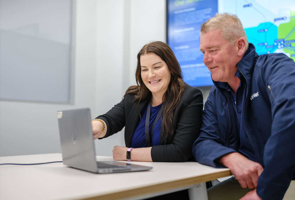 A woman and man smiling while looking at a laptop