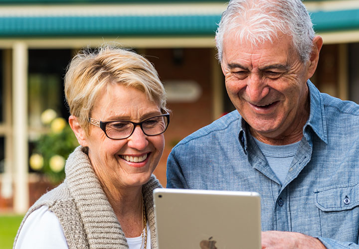 A smiling elderly couple looking at an ipad together