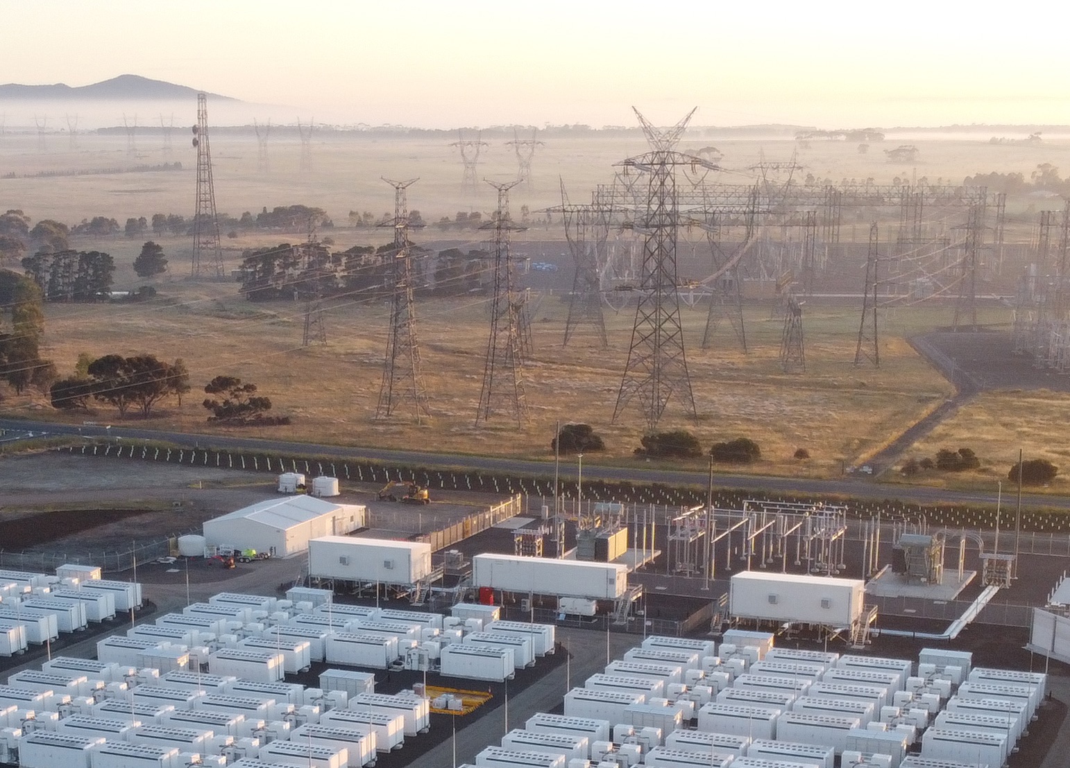 A long row of transmission towers next to a large battery storage system