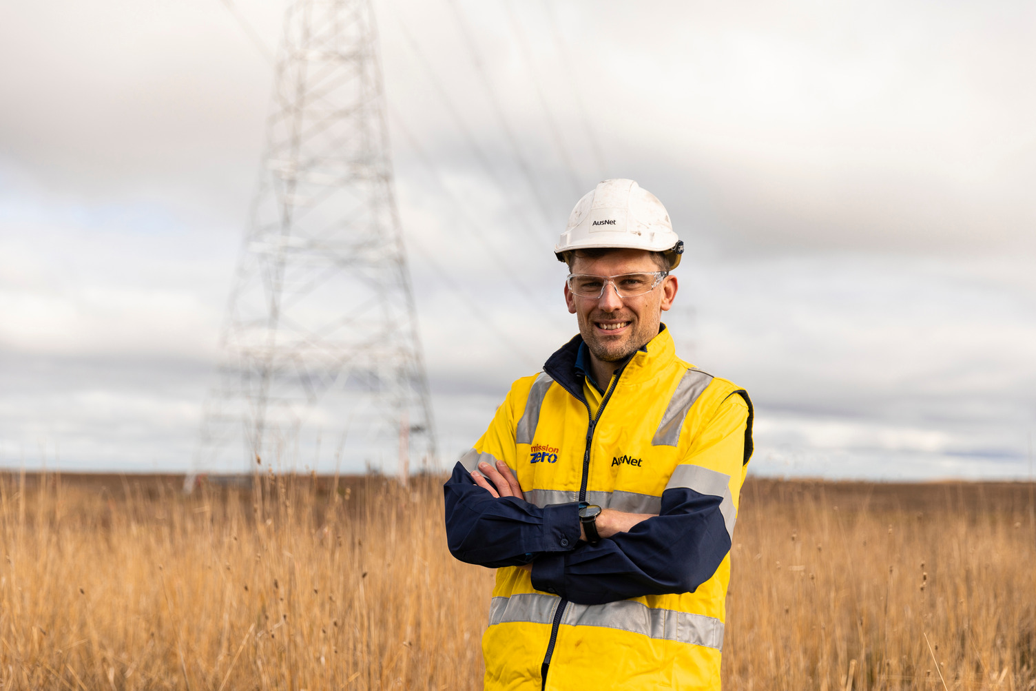 A man in high-vis smiling in front of a transmission tower in a field