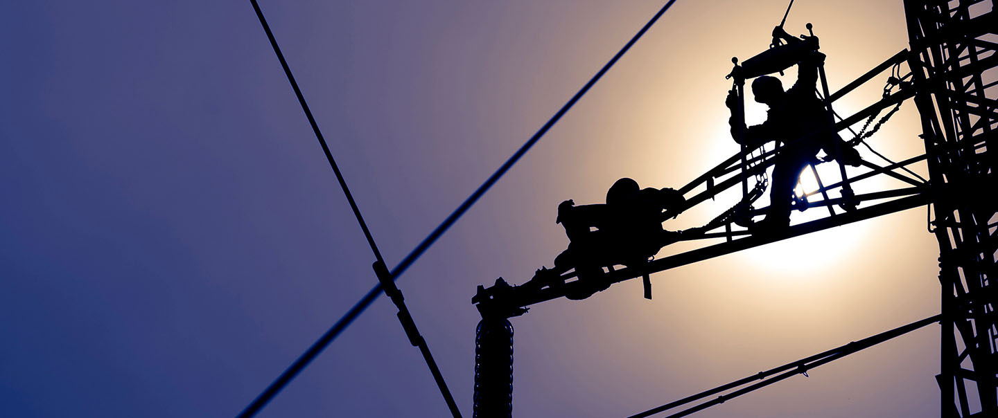View from below of two people working on an electrical line 