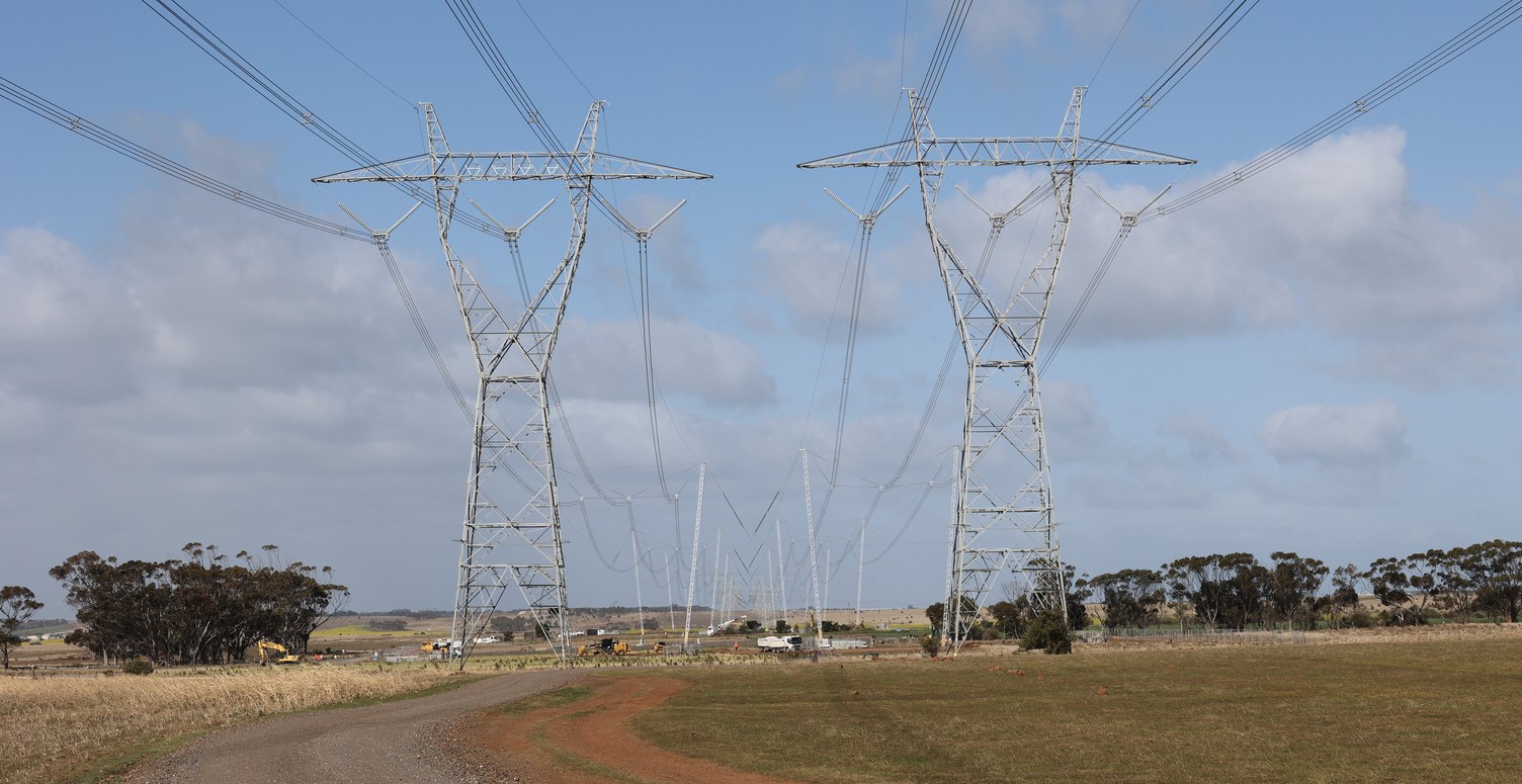Two rows of large electricity transmission towers across a field