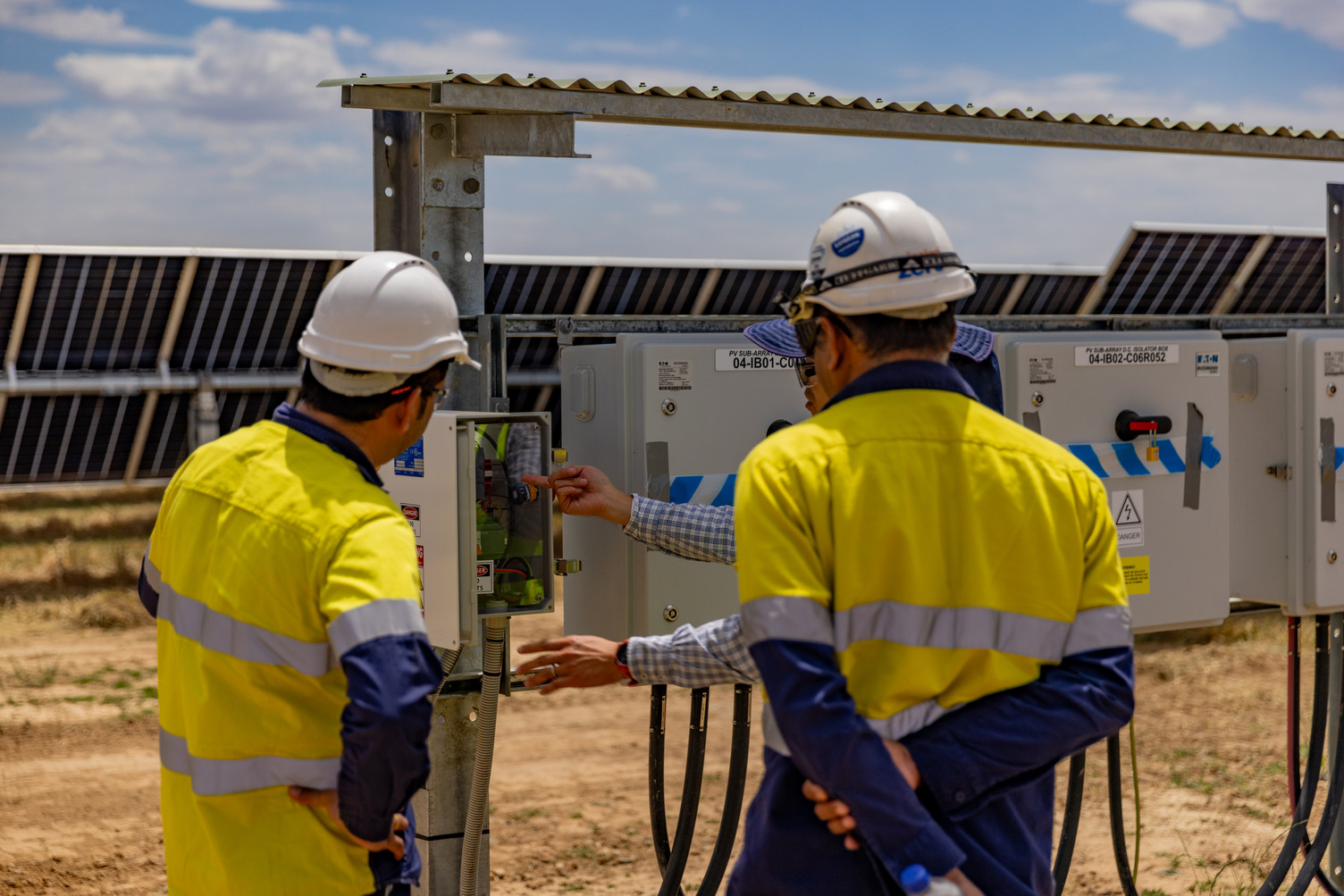 Two workers at a solar farm looking at solar equipment