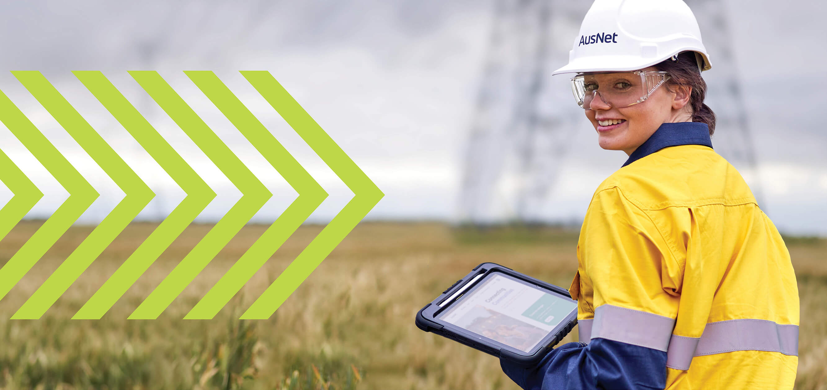 A smiling woman in high-vis near a large electricity transmission tower