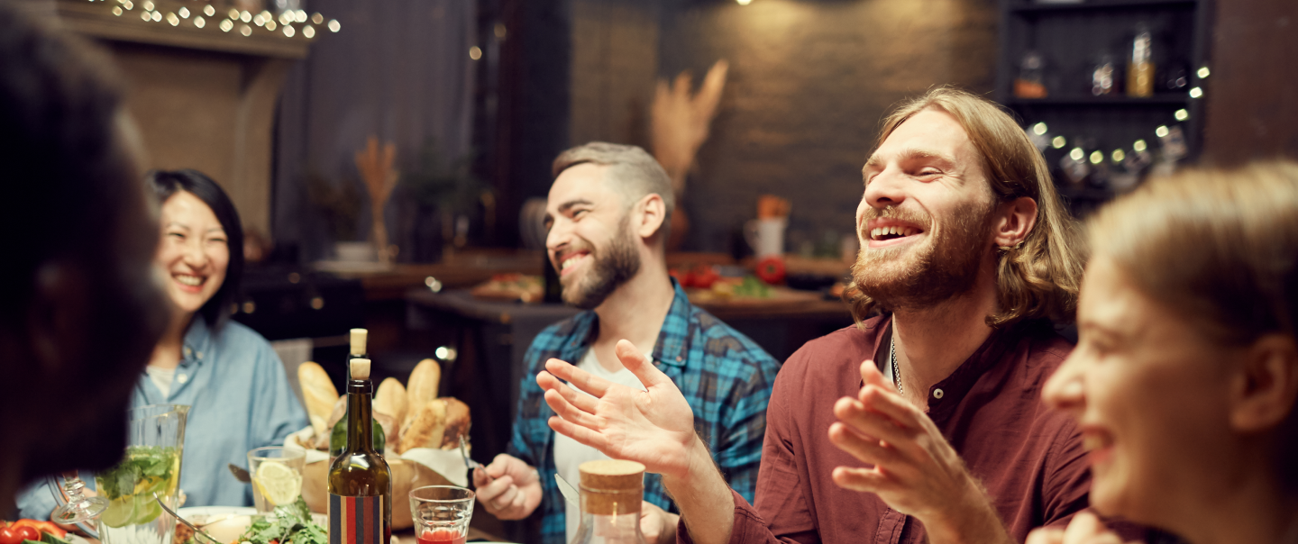 group of happy people sitting around a table with food and wine 