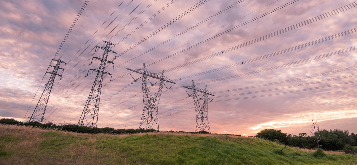 Four electricity tranmission lines spanning across a field at dusk