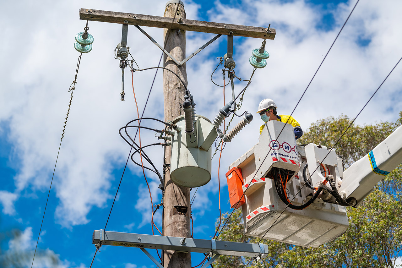 technician wearing hard hat, high vis and safety harness servicing a transmission line