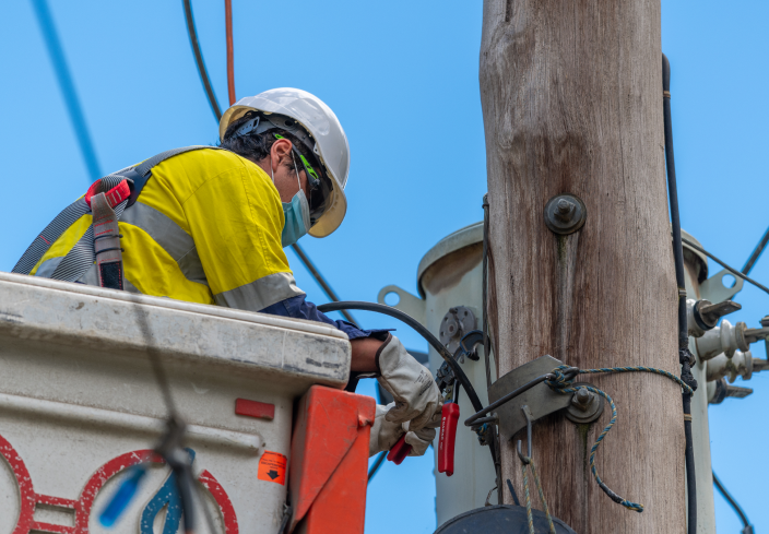 technician wearing hard hat, high vis and safety harness servicing a transmission line