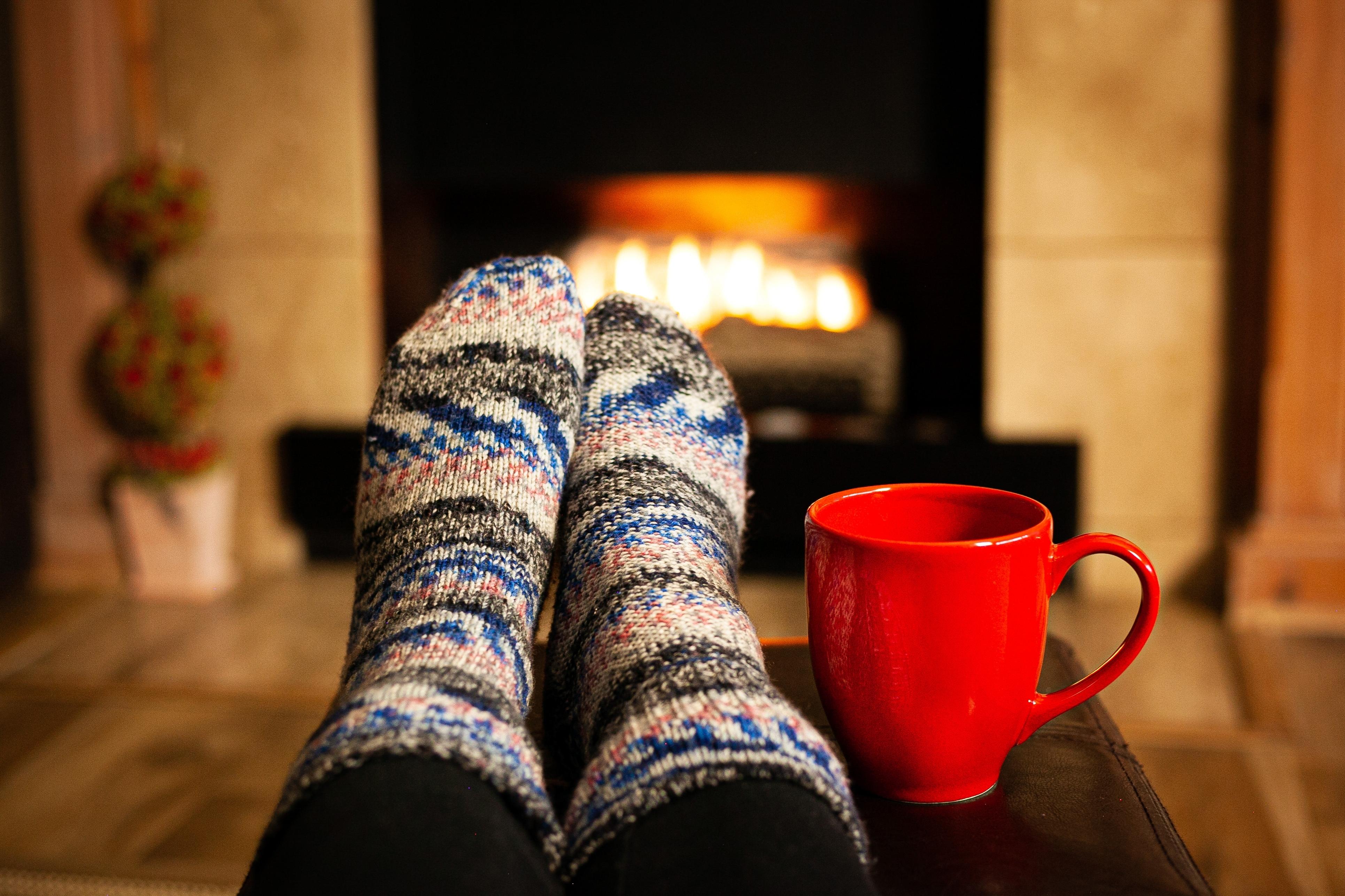 Picture of a persons feet in warm socks in front of a fire with a red mug